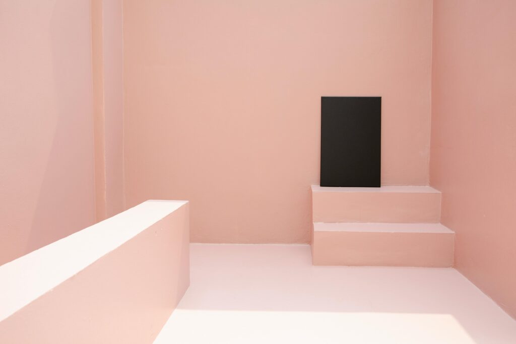 A modern minimalist pink room featuring a black canvas on small steps.